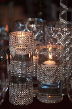 Two lit candles in glass holders with a reflective pattern.