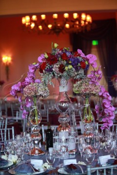 Elegant floral centerpiece with vibrant red, purple, and pink flowers on a glass stand.