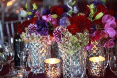 Elegant crystal vases with vibrant flowers and glowing candles on a table.