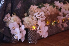 Elegant white orchids and roses in crystal vases with soft candlelight.