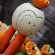 Carved white pumpkin with a face and orange fruit decoration.
