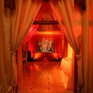 Elegant red-lit event space with draped curtains and candlelight.