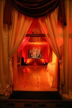Elegant red-lit event space with draped curtains and candlelight.