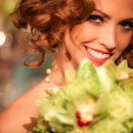 Smiling woman with curly red hair holding a bouquet of flowers.