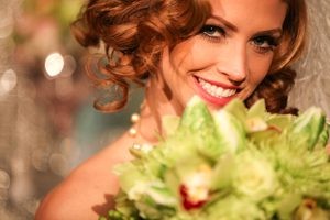 Smiling woman with curly red hair holding a bouquet of flowers.