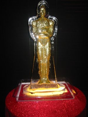 Golden Oscar statuette encased in clear display box on red base.