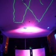 Colorful laser lights create vibrant shapes on a ceiling in a dark room.