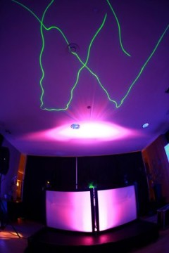 Colorful laser lights create vibrant shapes on a ceiling in a dark room.
