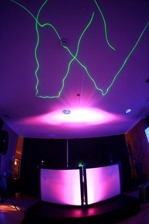 Colorful laser lights create vibrant shapes on a ceiling in a dark room.