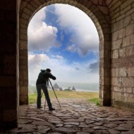 Photographer capturing a scenic landscape through a stone archway.
