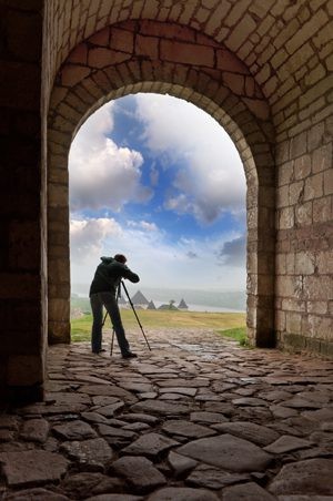 Photographer capturing a scenic landscape through a stone archway.