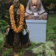 A statue adorned with a marigold garland in a serene garden setting.