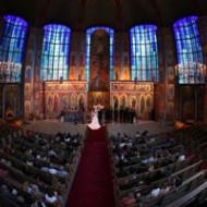 A couple exchanging vows in a grand, ornately decorated church filled with guests.