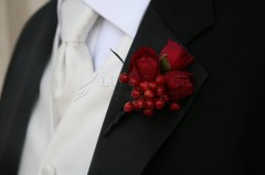 Close-up of a groom's boutonniere with red berries and flowers on a black suit lapel.