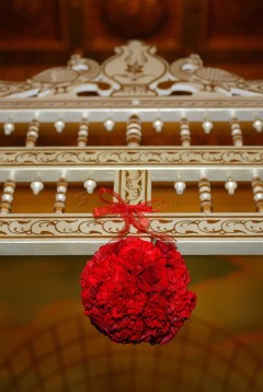 Red floral ball decoration hanging with a bow on ornate white railing.