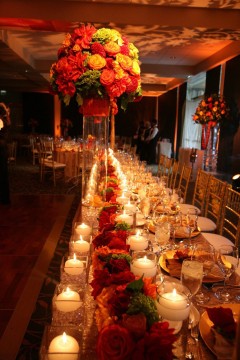 Elegant candlelit table with red floral centerpieces at a formal event.