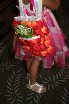 Child holding a bouquet of lilies of the valley, wearing a colorful dress with petals.