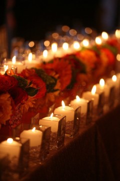 Row of lit candles with red roses in a dim setting.