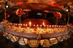 Elegant banquet table set with candles and floral centerpieces in a warmly lit venue.