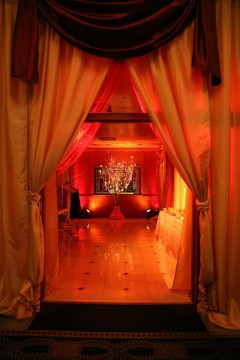 Warm, intimate room lit with red and orange hues, framed by flowing curtains.