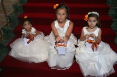 Three young girls in white dresses sitting with flower baskets.