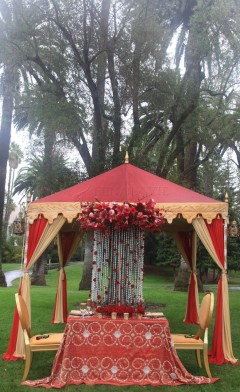 Elegant outdoor wedding mandap decorated with red and cream drapes and flowers.