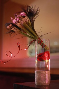 A delicate flower arrangement in a glass of water with curled red ribbons.