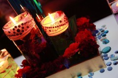 Lit candles surrounded by red flowers in a dim setting.