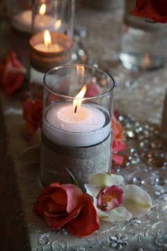 A floating candle lit inside a glass with decorative stones and flowers.