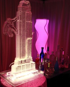 Illuminated ice sculpture of a building with a dragon figure, surrounded by colorful bottles and a glowing lamp.