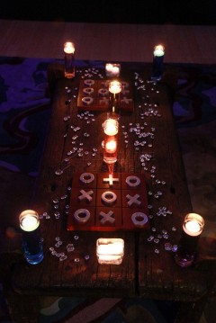 A dimly lit tic-tac-toe game with candles around it.