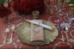 Elegant table setting with gold charger, beige napkin, and floral centerpiece.