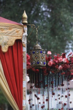 Intricately designed lantern hanging beside red drapes and floral decorations.