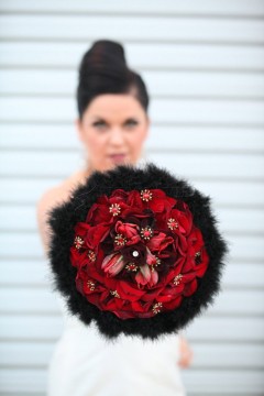 Bride holding a vibrant red floral bouquet with black accents.