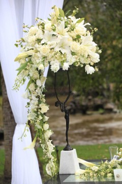Elegant floral arrangement with white orchids on a decorative stand outdoors.