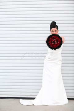 Bride in white holding a red and black bouquet against a white backdrop.
