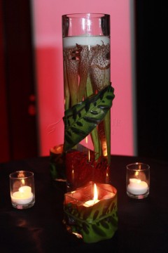 A green leaf centerpiece in a tall vase surrounded by three lit candles.