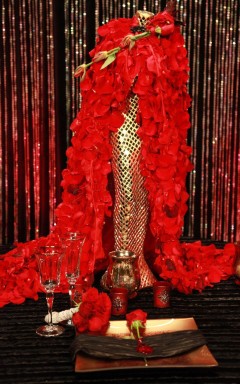 A glamorous gold sequined dress with a red feather boa on a mannequin.