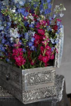 Vibrant purple and blue flowers arranged in an ornate silver box.