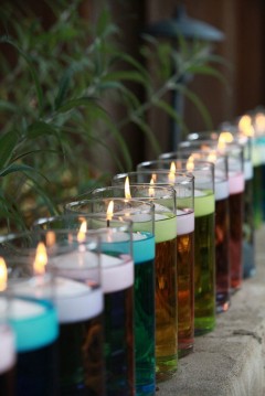 Colorful candles burning in a row with greenery in background.