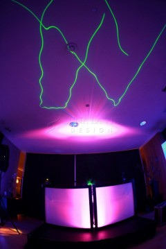 Room lit with vibrant purple and green laser lights creating abstract shapes.
