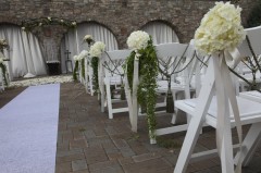 White chairs decorated with floral arrangements for an outdoor event.