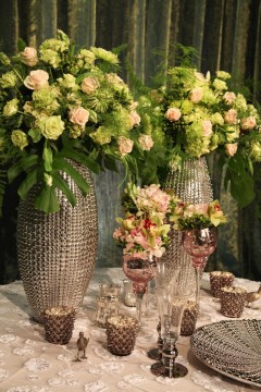 Elegant floral arrangements in large textured vases with crystal glassware on a table.