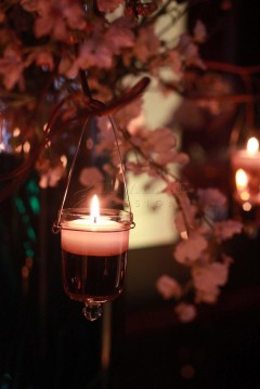A glowing candle in a glass holder surrounded by soft floral decor.