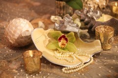 Elegant orchid and pearls on a decorative shell plate with candles.