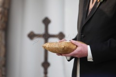 Person holding a golden decorated loaf of bread near a cross.