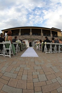 Outdoor wedding ceremony setup with guests seated facing a stone building.