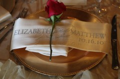 A rose placed on a folded napkin with wedding details on a plate.