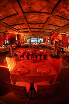 Elegant banquet hall with warm red lighting and floral centerpieces.