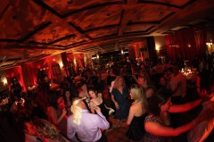 A lively party with people dancing and socializing under warm red lighting.